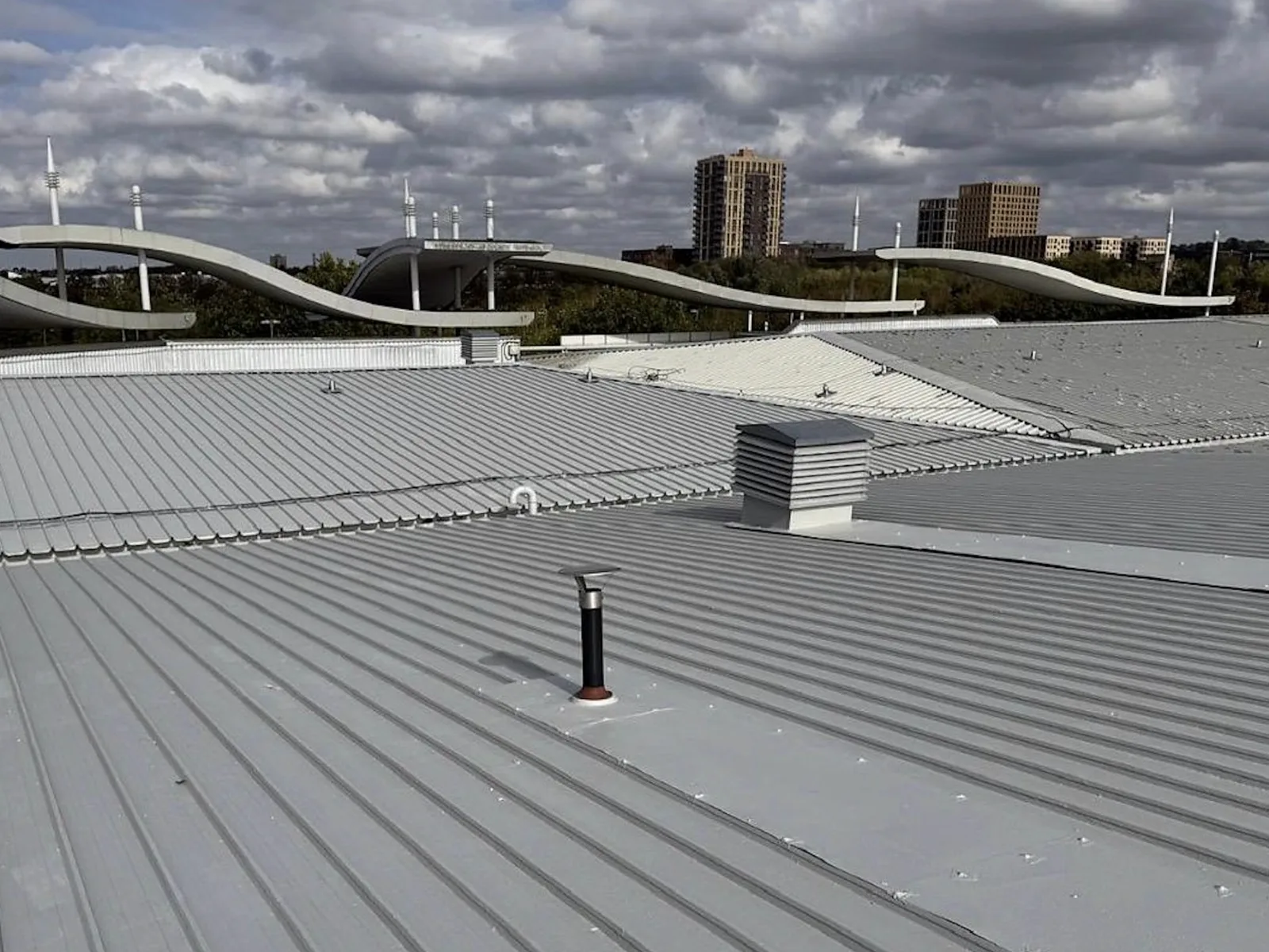 Wide view across a refurbished profiled commercial roof with vents and roof-level structures