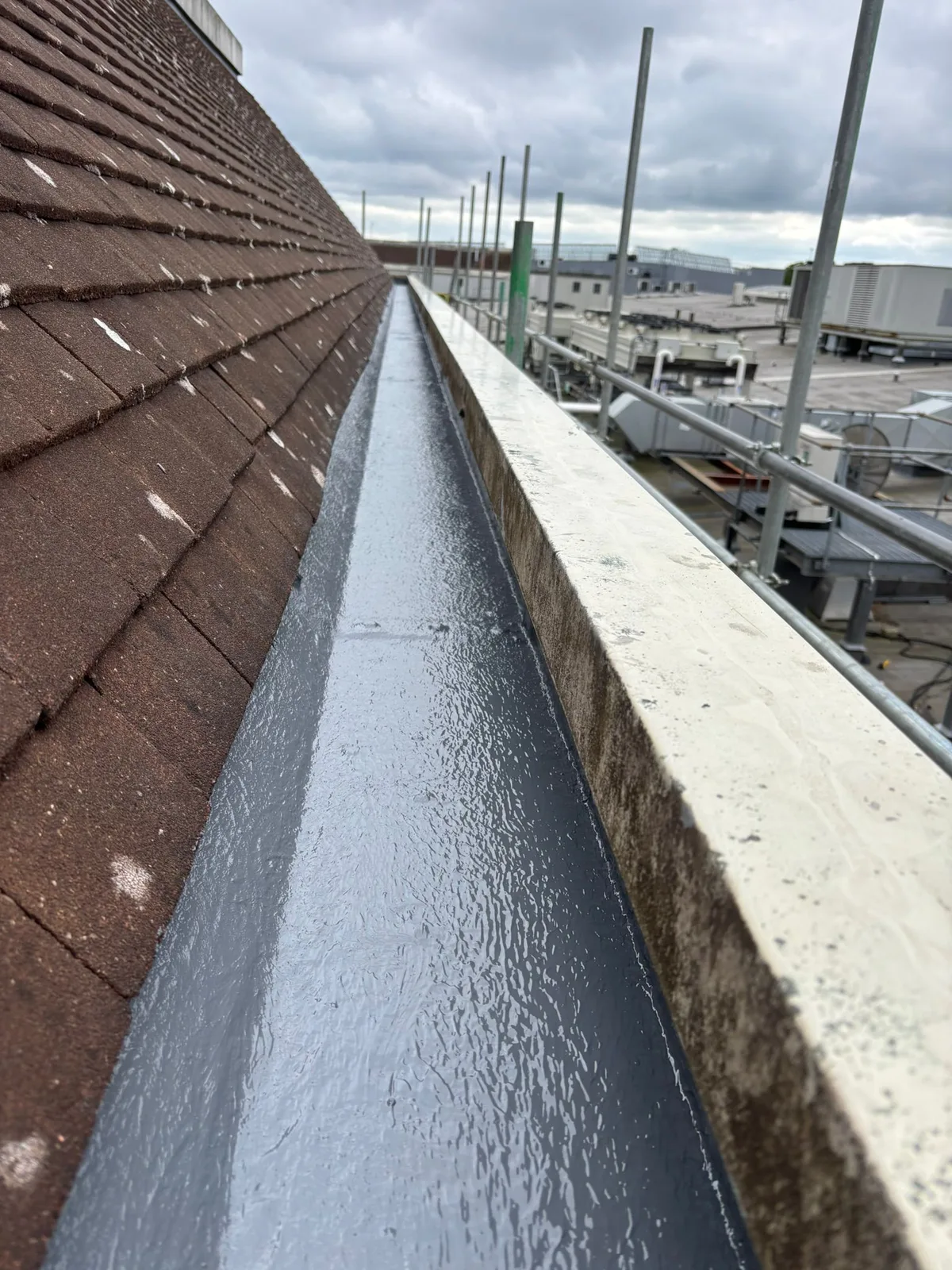 Liquid-applied lining within a commercial gutter. Gutter geometry, outlets and substrate condition are checked at survey.